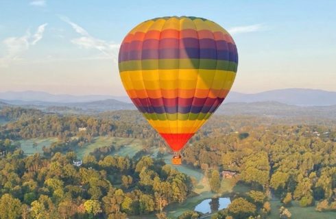 Rainbow colored hot air balloon suspending in the sky over a large valley dense with trees