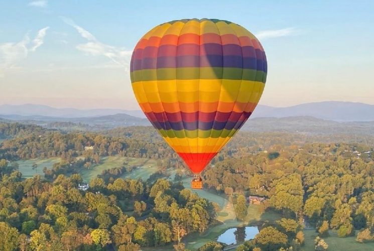 Rainbow colored hot air balloon suspending in the sky over a large valley dense with trees
