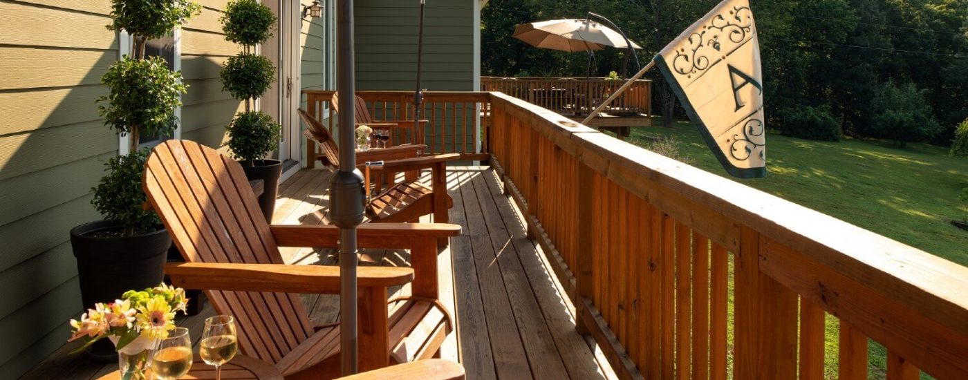 Outdoor deck with four adirondack chairs overlooking a lawn surrounded by trees