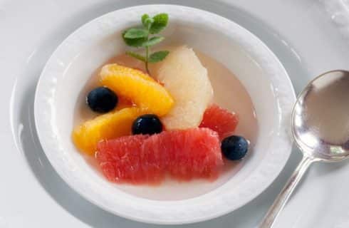 Small white bowl wth sliced oranges and grapefruit, blueberries and sprig of mint