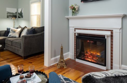 Sitting area of a bedroom with sectional couch, sitting chairs and gas fireplace with white mantel