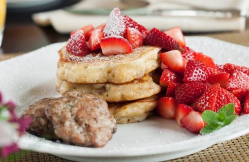 White breakfast plate of pancakes covered in fresh sliced strawberries and powdered sugar