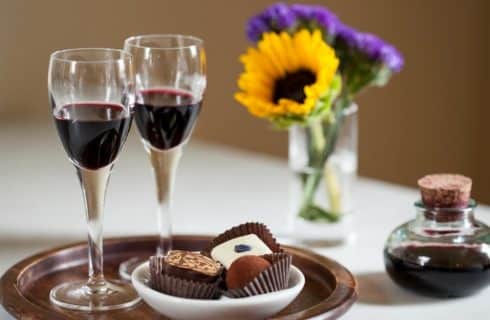 Wooden plate with two glasses of red wine and three chocolate truffles