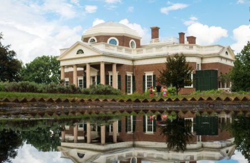 Stately brick historic building with many windows and columns in front of a pond