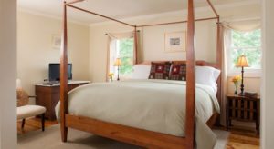 Bright and airy bedroom with four poster bed, dresser with TV and large windows