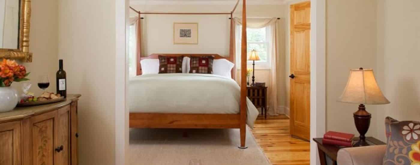 Sitting area with tan loveseat and coffee table with doorway showing large four poster bed