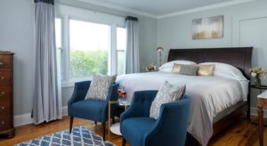 Elegant bedroom with king bed, dark wood headboard, large picture window and two blue club chairs