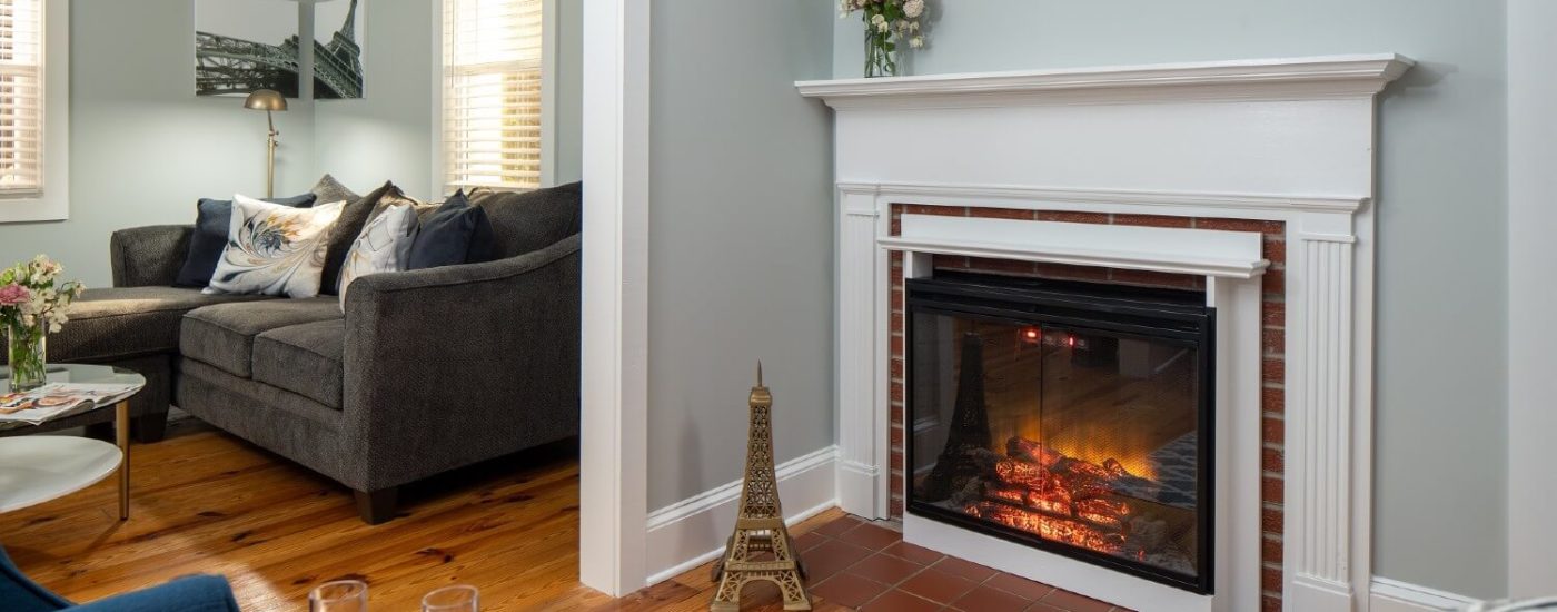 Sitting area of a bedroom with sectional couch, sitting chairs and gas fireplace with white mantel