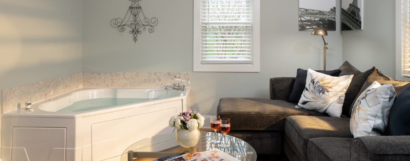 Small room with grey sectional couch, round glass coffee table and corner jacuzzi tub