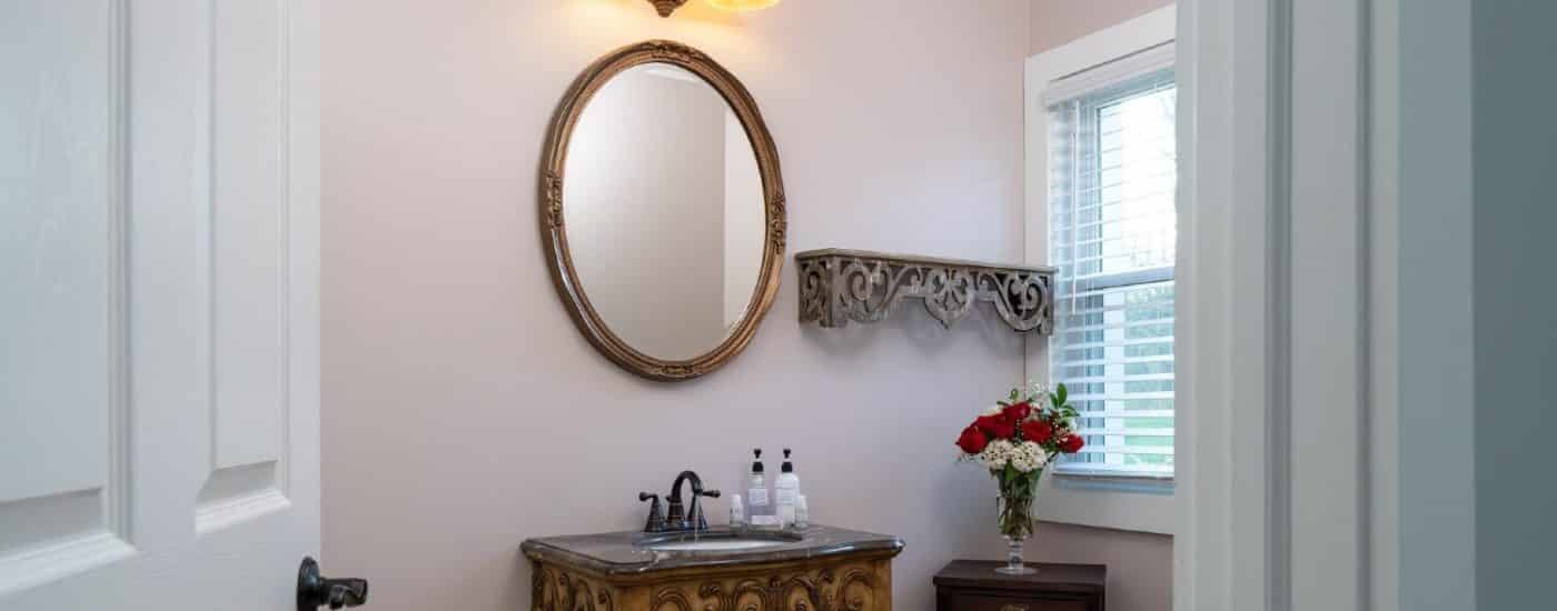 Bathroom with antique style vanity, framed round mirror and side table with vase of roses