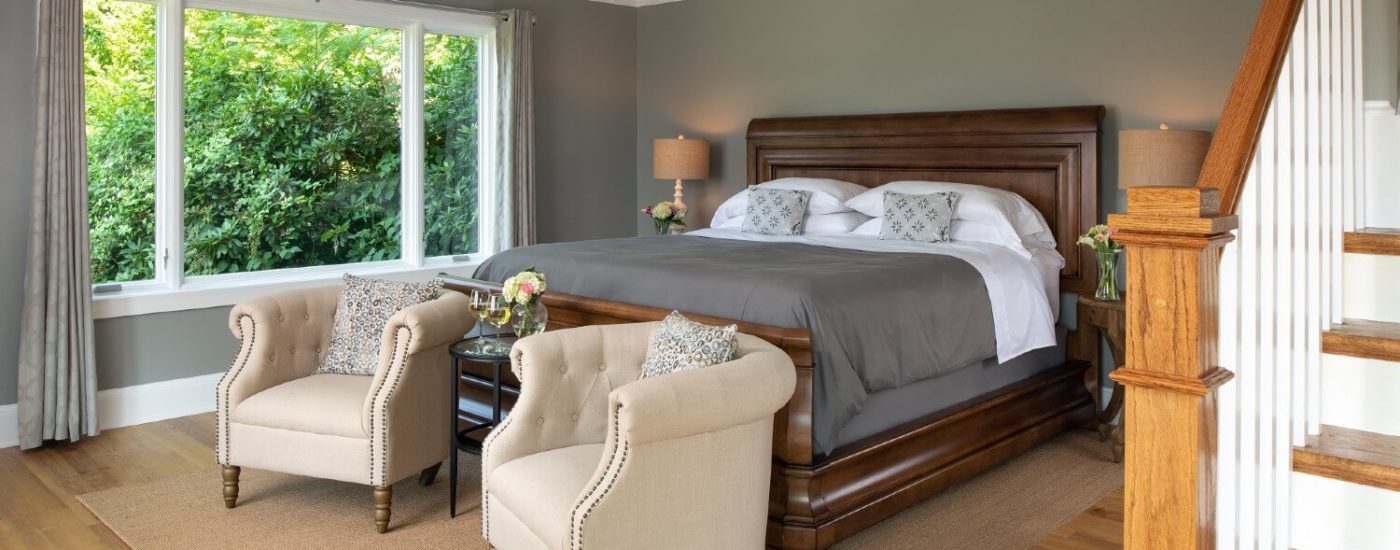 Large guestroom with king sleigh bed, large picture window and two beige club chairs