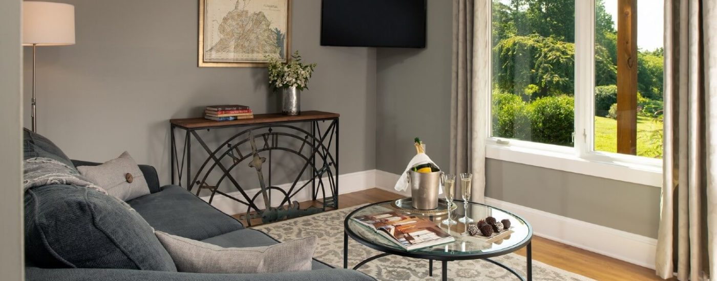 Sitting area with grey loveseat, round glass coffee table, corner TV and large picture window