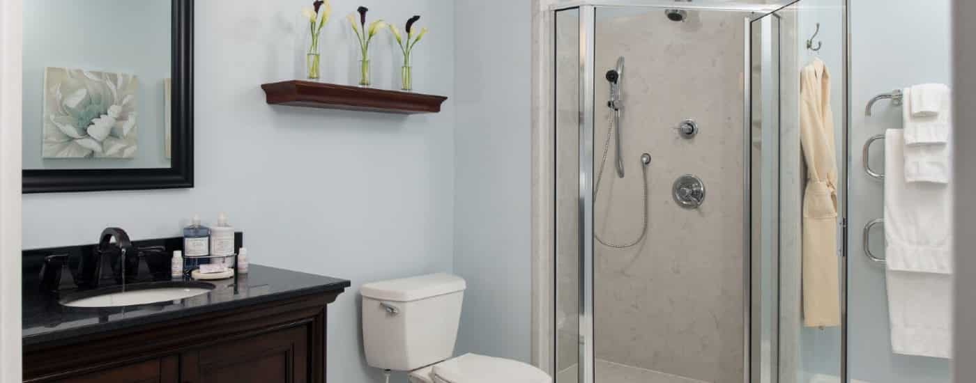 Spacious bathroom with corner stand up shower, rack of white towels, toilet and single sink vanity