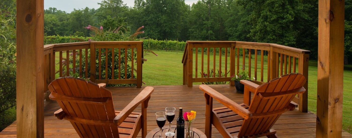 Outdoor deck with two adirondack chairs and table with wine, glasses and vase of flowers