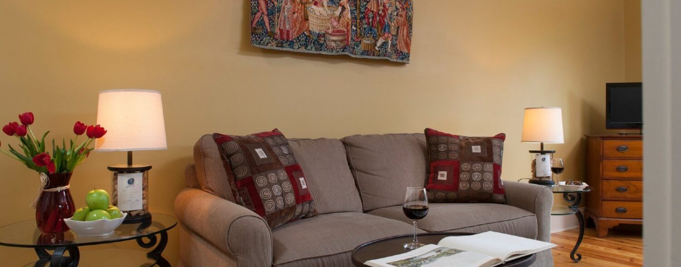 Sitting area with grey loveseat, glass side table with lamp, flowers and bowl of apples