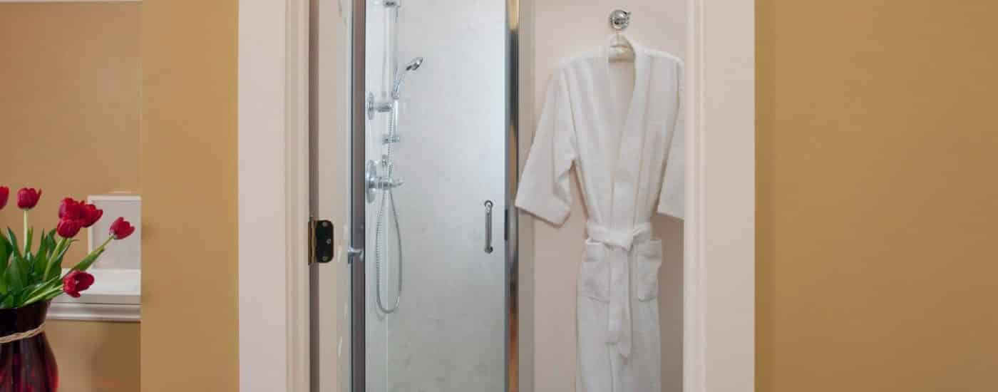 Bathroom with large stand up shower, hanging white robe and vase of red tulips