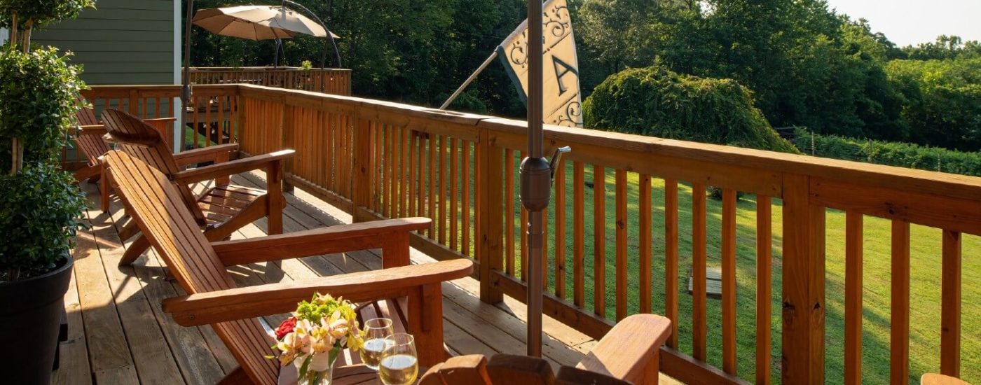 Outdoor deck with four adirondack chairs overlooking a lawn surrounded by trees