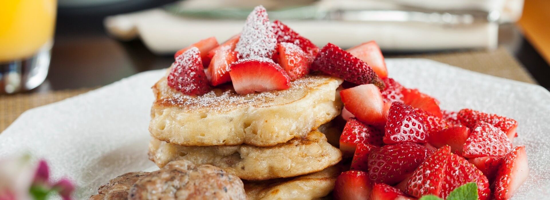 White breakfast plate of pancakes covered in fresh sliced strawberries and powdered sugar