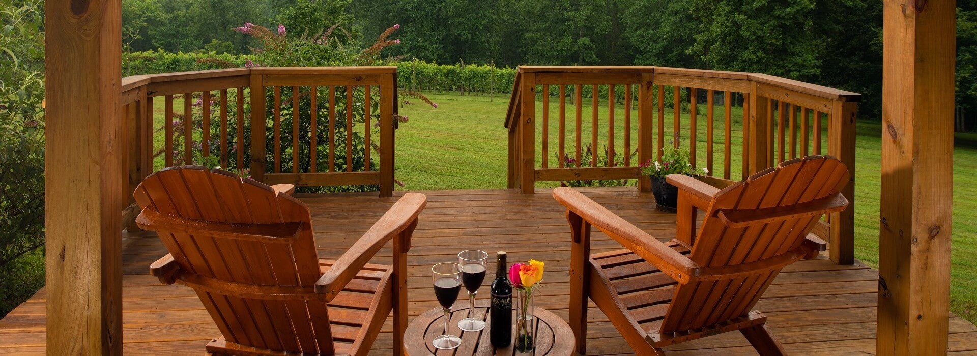 Outdoor wood deck with two Adirondack chairs and side table with bottle of wine, two glasses and vase of roses