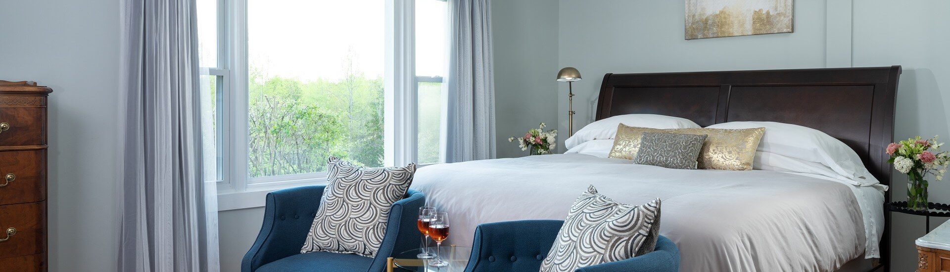 Bedroom with king bed in white linens, large picture window and two blue club sitting chairs