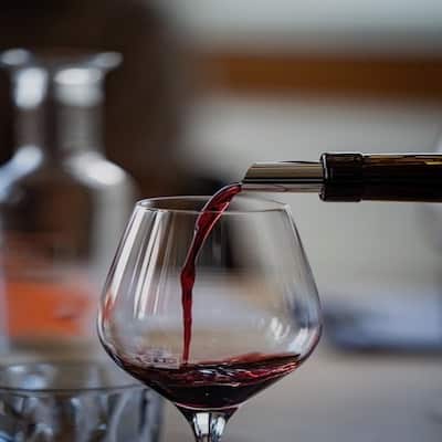 Red wine streams from a bottle into a wine glass, with a blurred bar in the background.