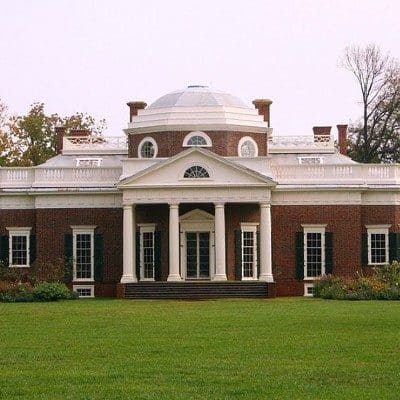 Stately historic brick home with white trim, large windows and front portico with columns