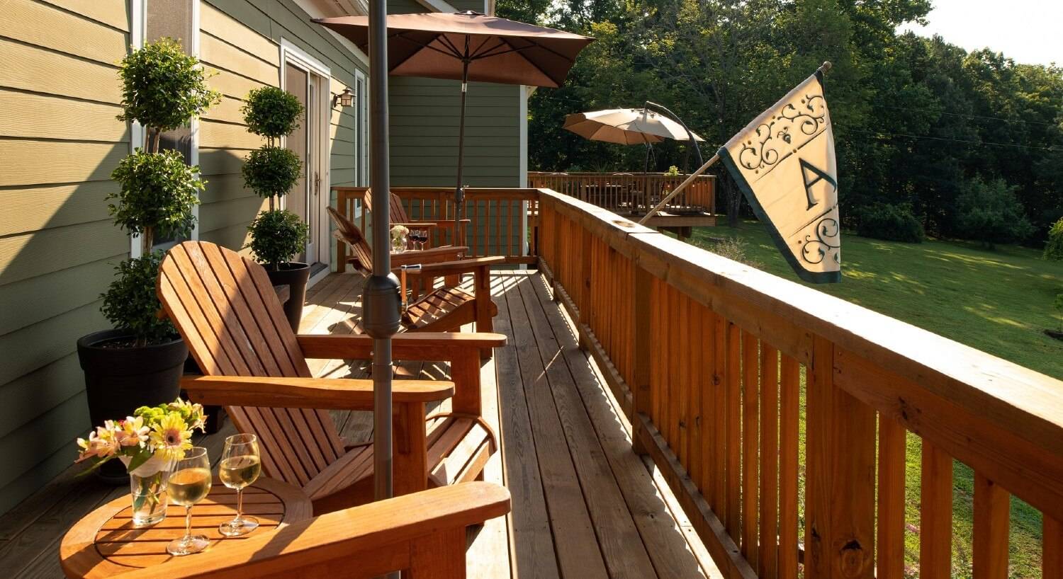 Outdoor deck with four adirondack chairs overlooking a lawn surrounded by trees