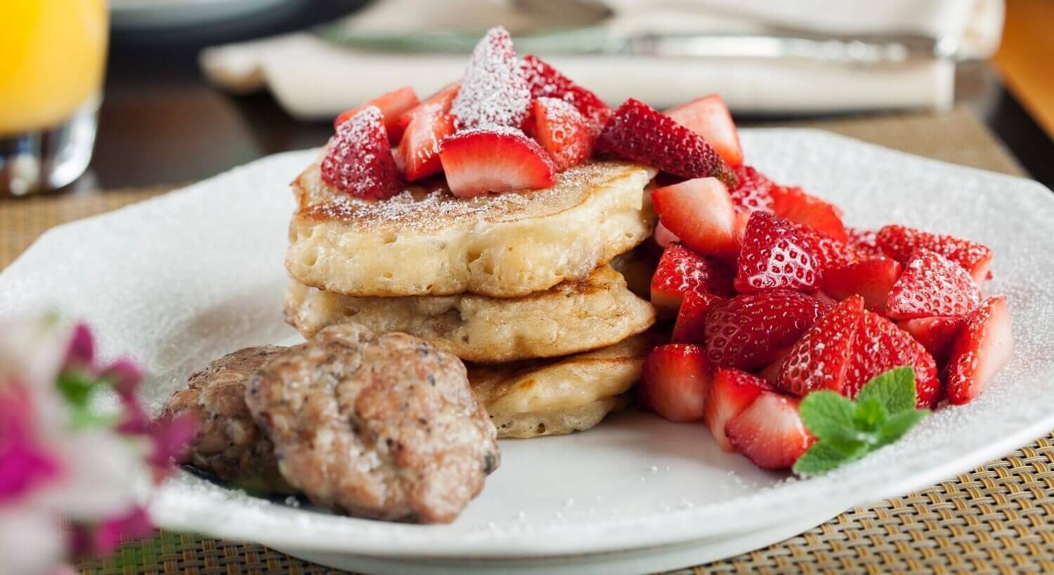 White breakfast plate of pancakes covered in fresh sliced strawberries and powdered sugar