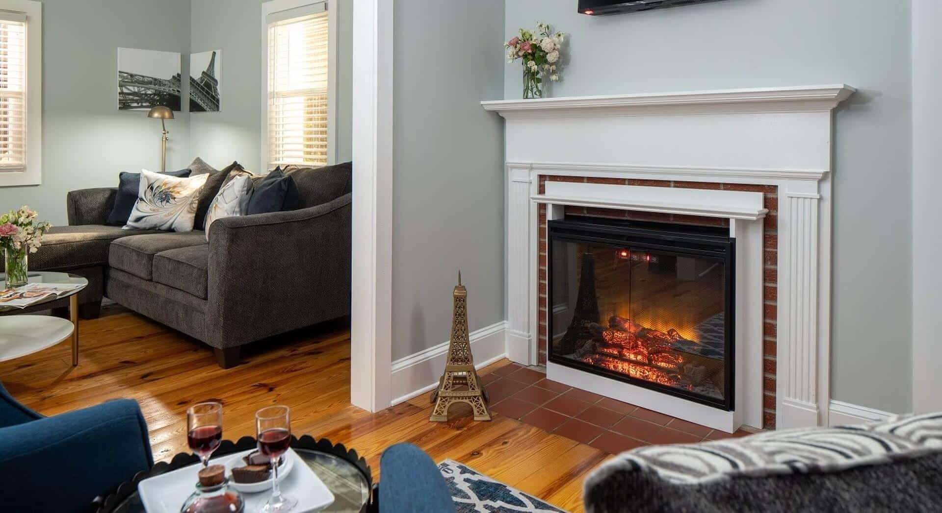 Sitting area of a bedroom with sectional couch, sitting chairs and gas fireplace with white mantel