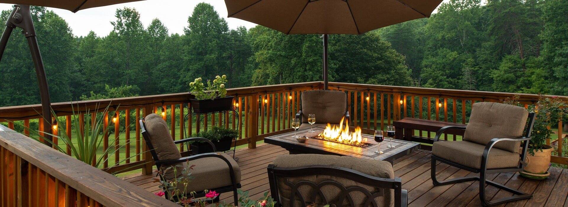 Outdoor patio overlooking woods and lawn with four chairs and gas fireplace coffee table