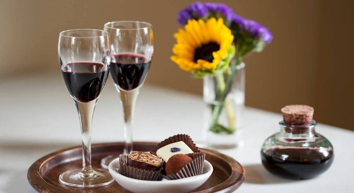 Wooden plate with two glasses of red wine and three chocolate truffles