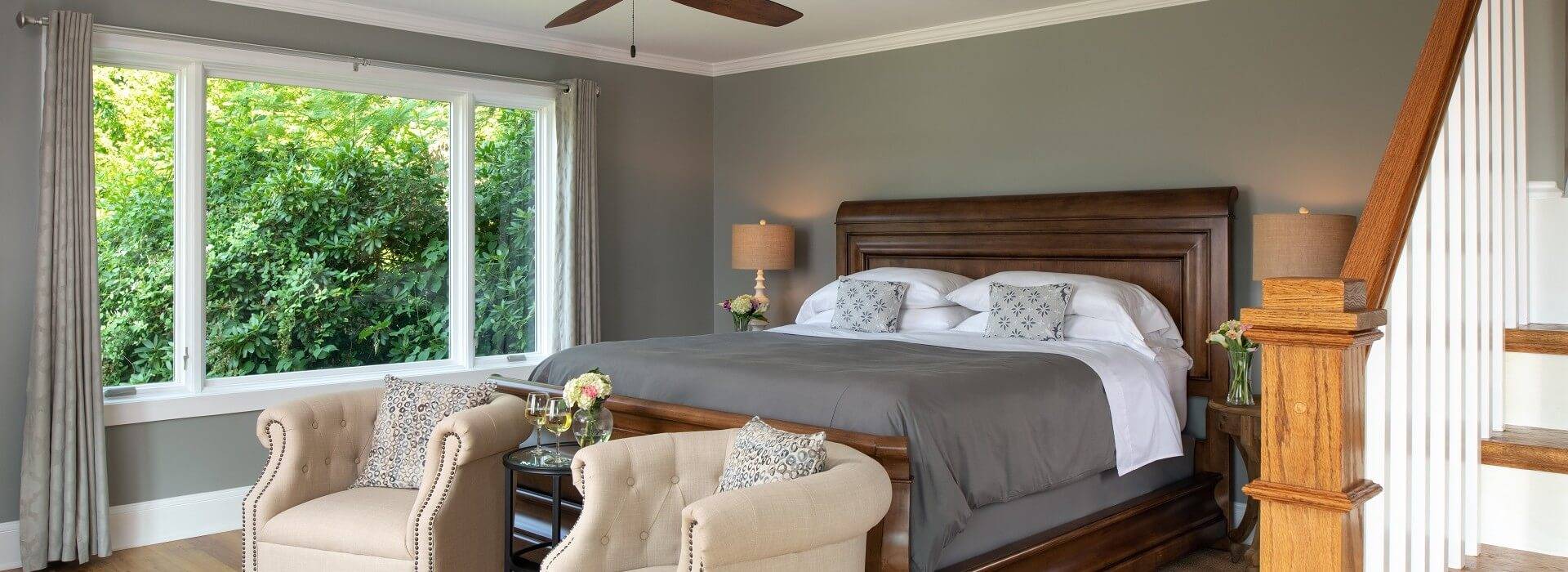 Large guestroom with king sleigh bed, large picture window and two beige club chairs